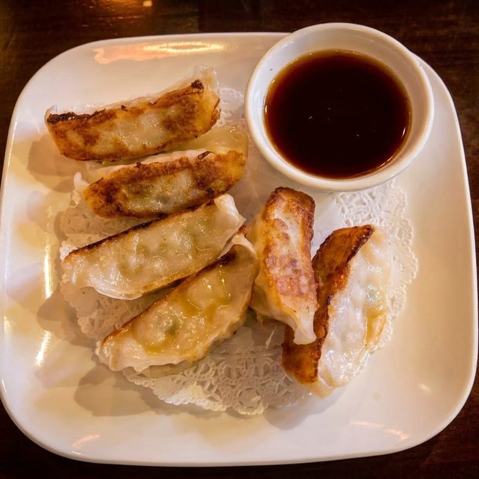 Pan-fried dumplings with a side of soy sauce on a white rectangular plate.